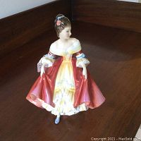 Photo showing front and side angle of Royal Doulton Southern Belle porcelain figurine dressed in red and yellow flowing dress with blue shoes and flower in hair.