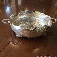 Side angle shot showing the overall shape, scalloped edge, and decorative handles of the fruit bowl on a wooden surface.