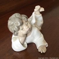 Front angled view of porcelain sleepy angel figurine lying on side, showing curled legs, closed eyes, and detailed facial features.
