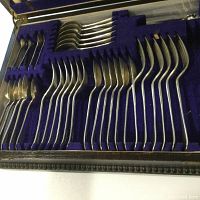 Top-down view of the silverplate flatware set neatly arranged in blue velvet-lined compartments of the hardwood box, showing spoons, forks, and other utensils.