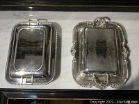Top down photo of two silver plated lidded entree dishes on a marble surface.