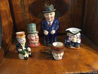 Photo showing five collectible figurines of various sizes including the large Royal Crown Derby Cliff Cornell figure and four smaller Dickens character figurines.