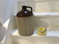Full view of large jug beside a cup and saucer for size reference, showing two-tone glaze and handle.