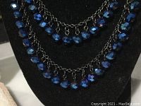 Close-up of the deep indigo faceted bead necklace on chain links underneath bust display