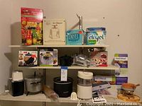Shelf with assorted kitchen items including crockpot, citrus juicer, chopper, vacuum sealer boxes, Dryel kits, ice shaver, chocolate fondue pot