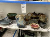 Wide shot showing the collection of pottery, 4 crocks with lids, bowls, mugs, plate.
