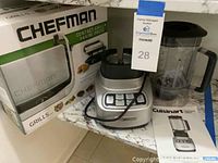 Overall view of the Chefman contact grill box next to the Cuisinart blender base and pitcher on a kitchen counter with instruction manual beside it.