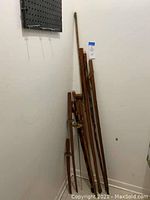 Several wooden walking sticks and wooden swords displayed upright against a wall.