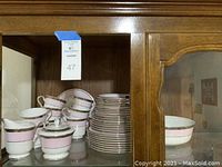 Overall view of mugs stacked alongside plates and saucers inside wood cabinet
