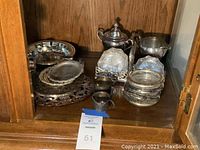 Cabinet shelf with assortment of silverplated trays, Roger Bros sugar and creamer set, coasters, FB Rogers dish, and trivets.