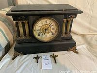 Full front view of Seth Thomas black mantel clock with decorative columns and gold-tone face, including two winding keys on the cloth surface.