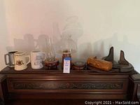 Wide view showing two ceramic beer steins, three lanterns, two wooden wall plate holders, and a wooden log with inside compartment on a carved wooden surface.