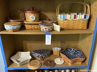 Front view of wooden shelving with multiple Longaberger baskets on two shelves, showing picnic basket on top right with cloth liner and star-shaped patriotic fabric baskets below.