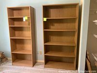 Two shelving units side-by-side against a light blue wall on carpeted floor. The taller unit has five shelves; the shorter unit has four shelves.