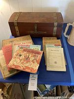 Full view of wooden box with various vintage books and pamphlets laid out in front on blue table.