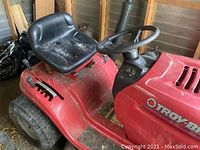 Side view of red Troy-Bilt riding lawn mower showing seat, steering wheel, and control levers.