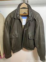 Front view of the dark brown men's leather jacket on hanger showing collar, pockets and zip.