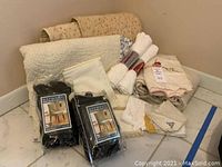 Overview of quilts, cotton blanket, packaged chair covers, and linens on white floor in corner