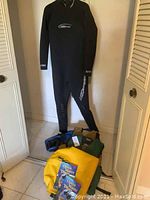 Full view of black Neosport wetsuit hanging with dive fins, life jackets, SealLine dry bag, and two diving instruction books on the floor.