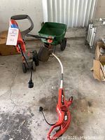 Wide view of edger, weed eater, and fertilizer spreader on concrete floor showing all three items together