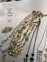 Assorted Mary Kay costume jewelry including pearl-like beaded necklace, gold-tone necklace, rhinestone brooch in shape of a crown, silver necklace with pendant, and additional jewelry