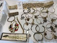 Top-down photo showing numerous silver-tone Mary Kay charm bracelets, a multicolor charm bracelet, a star bracelet, and a braided belt.
