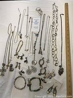 Full display of assorted necklaces, bracelets, and earrings arranged on a white cloth with a ruler for scale, showing the variety of items included in the lot.