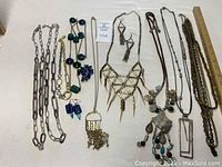 Overview of 9 long necklaces laid flat including various metals, beads and pendants.
