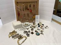 Full view of lot showing earrings on wooden display, rings with dish and jewelry box, tie bars laid out