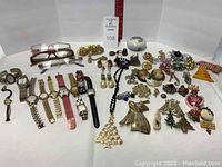 Full view of assorted watches, pins, earrings, reading glasses and Christmas necklace and pins laid on white background.