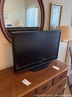 Black framed 32-inch LCD television model LC321559A placed on wooden furniture with oval black stand base, no remote visible.