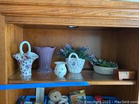 Shelf displaying floral patterned, lavender, and cream vases, white ceramic basket with faux lavender flowers, faux succulent dish, and wooden trinket box.