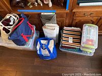 Wide shot showing multiple bags, clear bins, bolts and stacks of fabric placed on floor in front of wood cabinets.