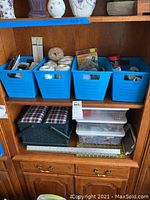 Shelf with multiple blue plastic bins filled with sewing accessories, basket, and clear plastic containers with more supplies on the shelf below