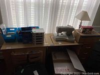 Full view of wooden sewing table with machine recessed in drop-in compartment and various accessories on top (not included)