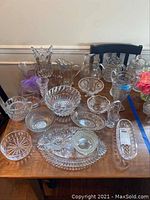 Full view of the entire lot showing a variety of glassware items including vases, pitchers, bowls, platters, and dishes arranged on wooden table.