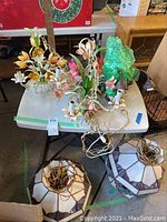 Four chandeliers on table including two metal floral and two stained glass chandeliers