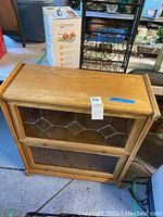 Front view of wooden barrister bookcase with a top compartment that has a leaded glass door and a lower compartment door below, both doors lift up.