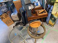 Round patio table with metal frame and glass top alongside the round wooden side table with loose glass top, and wooden tray table with some items on it