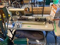 Two Lifetime brand plastic folding tables with beige or light gray tops and black foldable legs, photographed in a garage setting with various items on and around them.