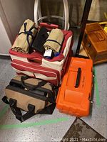 Overview of the lot showing rolling canvas tool chest, black canvas tool bag, orange plastic toolbox, two rolled canvas tool wraps, and wooden box.