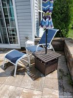 View of the adjustable patio chair and ottoman with the drum table and umbrella set up outside on a stone patio.