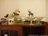 Overall view of horse decor, ceramic horse figurine, uranium glass and depression glass pieces on top of a wooden cabinet.