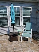 Full view of patio chair, umbrella with stand, metal drum table, and ottoman arranged on tiled patio against house wall.