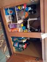 Cabinet with assorted cleaning products under kitchen sink including WD-40, detergents, cleaning brushes, and scrubbers