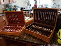 Two wooden chest boxes containing distinct Oneida Community flatware collections arranged on kitchen counter.