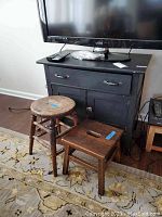 Vintage black painted wooden cabinet with single drawer, double doors, metal hardware, sitting on floor with TV on top.