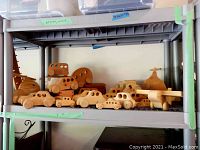 Shelf of natural finish wooden toys shaped as cars, planes, trains and helicopter.