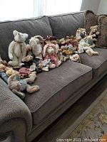 Photo showing about thirty stuffed bears and bunnies arranged on a couch, featuring a variety of clothing styles and sizes.