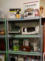 Metal shelving unit with boxed Ninja Master Prep food processor, boxed Crock-Pot slow cooker, Black & Decker toaster oven, small kitchen items, and various storage containers.